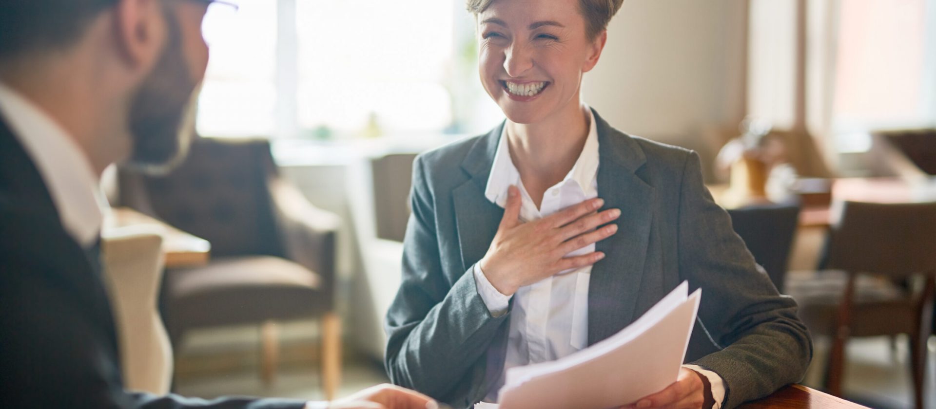 Laughing businesswoman with papers talking to her colleague during meeting in cafe