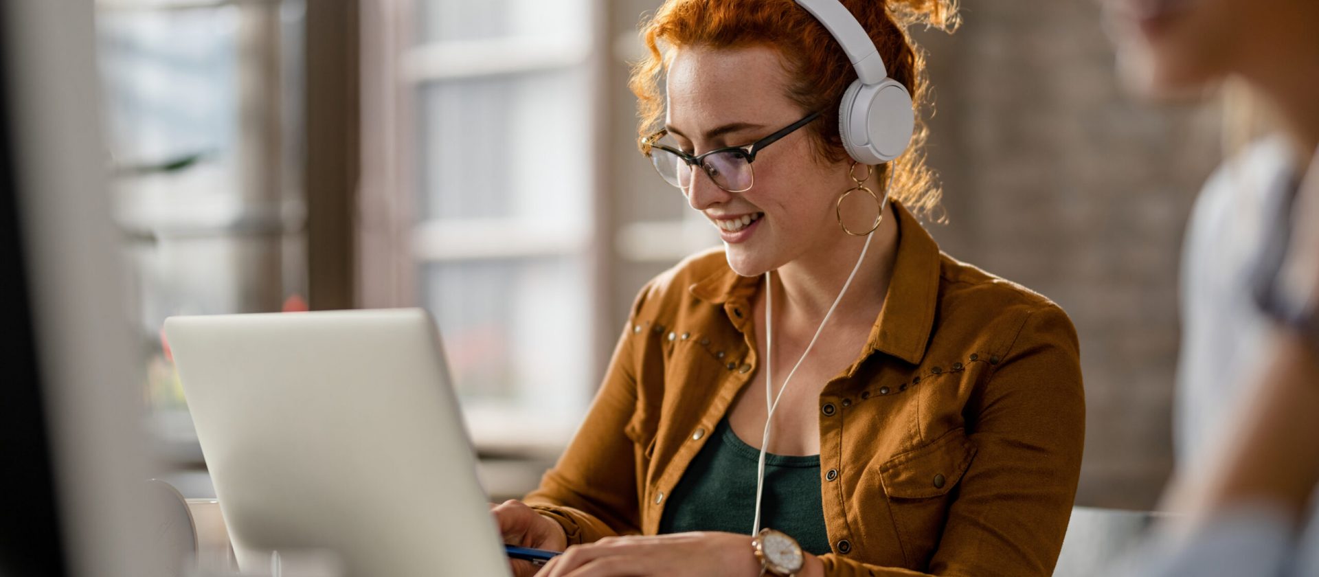 Smiling creative businesswoman listening music on headphones while working on a computer in the office.