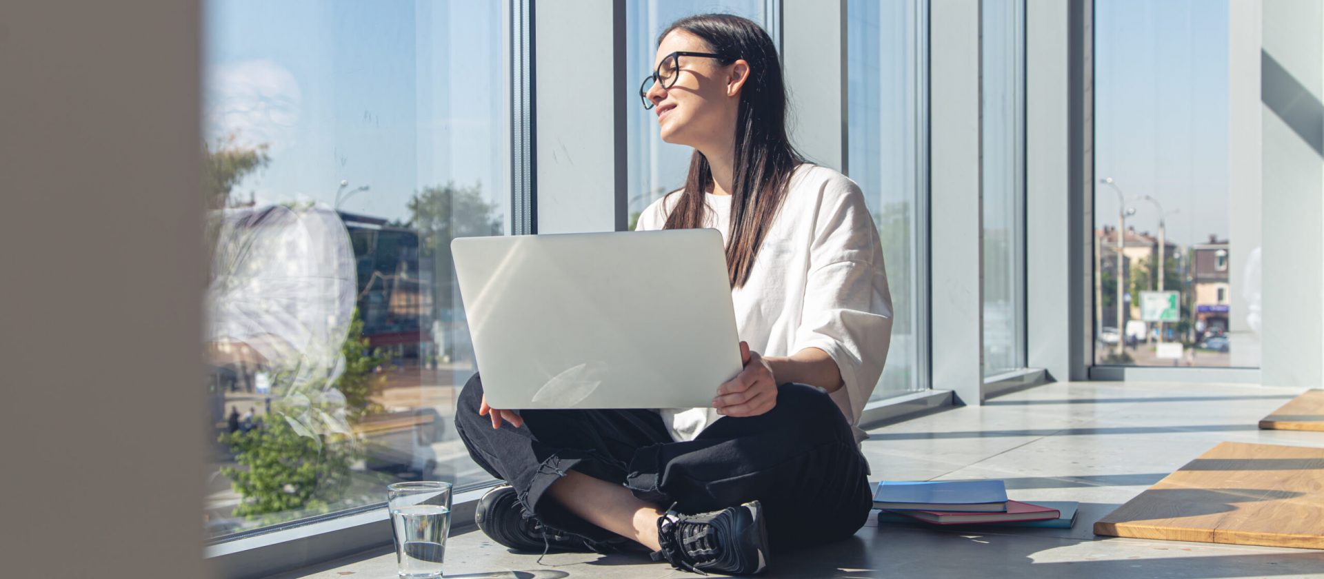 Young woman with a laptop at the window on a summer morning, working in a modern office.